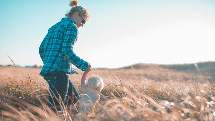 Mother walking hand-in-hand with her young child through a sunlit grassy field, evoking a warm, natural, and nurturing Mother’s Day moment.